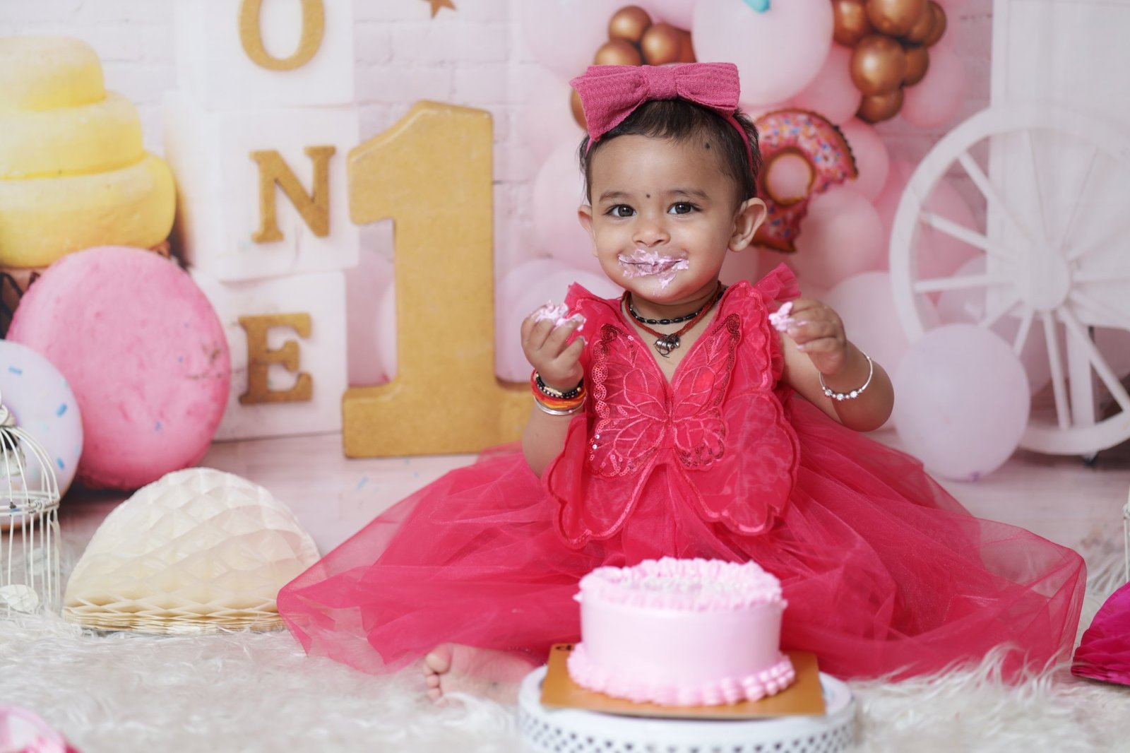 One year old sitting beside a birthday cake on a styled set