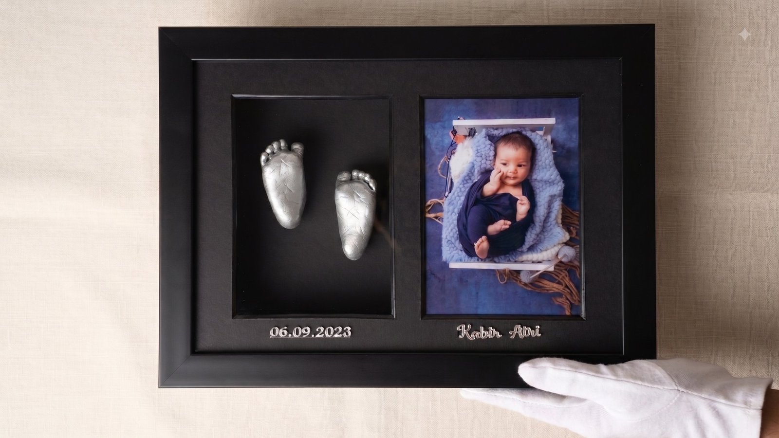 Black frame holding gold foot casts beside a newborn photograph