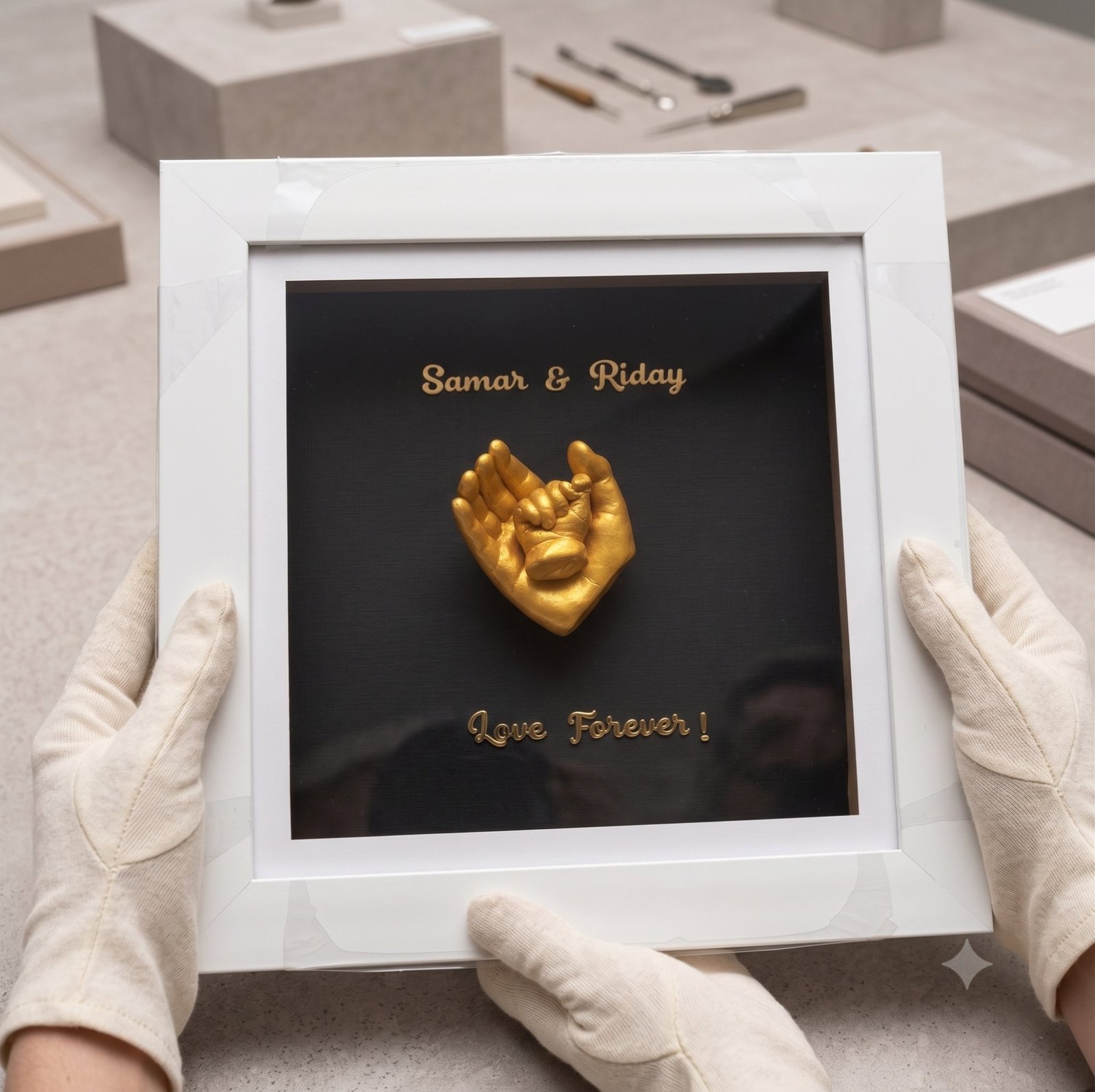 Two joined hands cast in gold and mounted in a white box frame