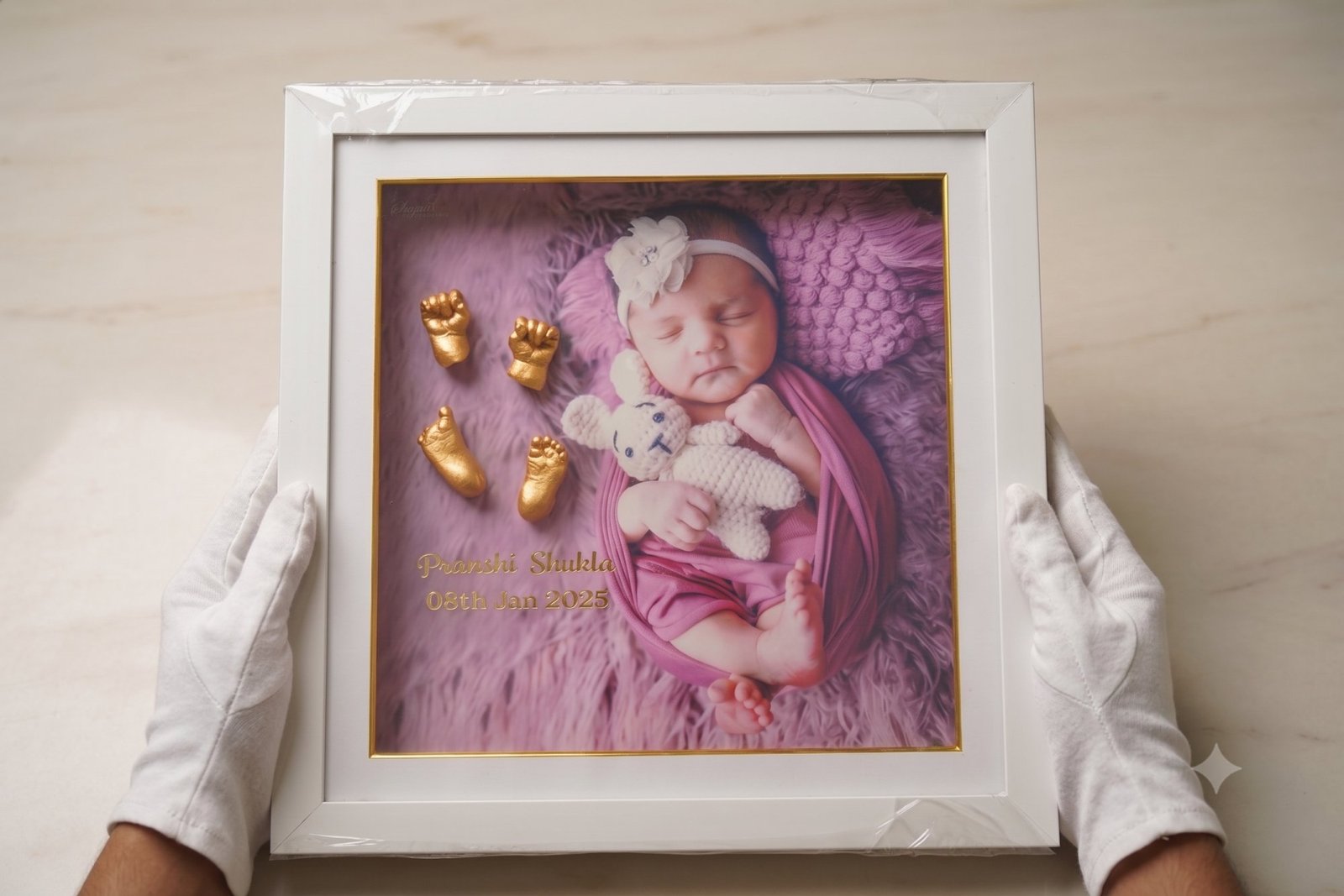 White frame pairing a gold hand cast with a newborn photograph