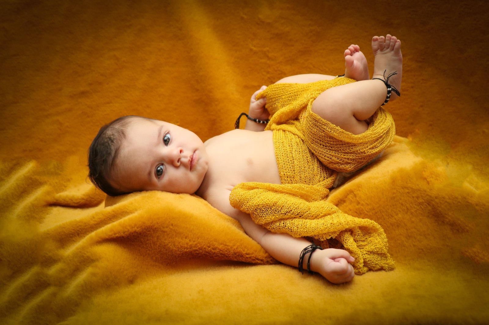 Baby lying on a mustard yellow blanket wrapped in matching fabric