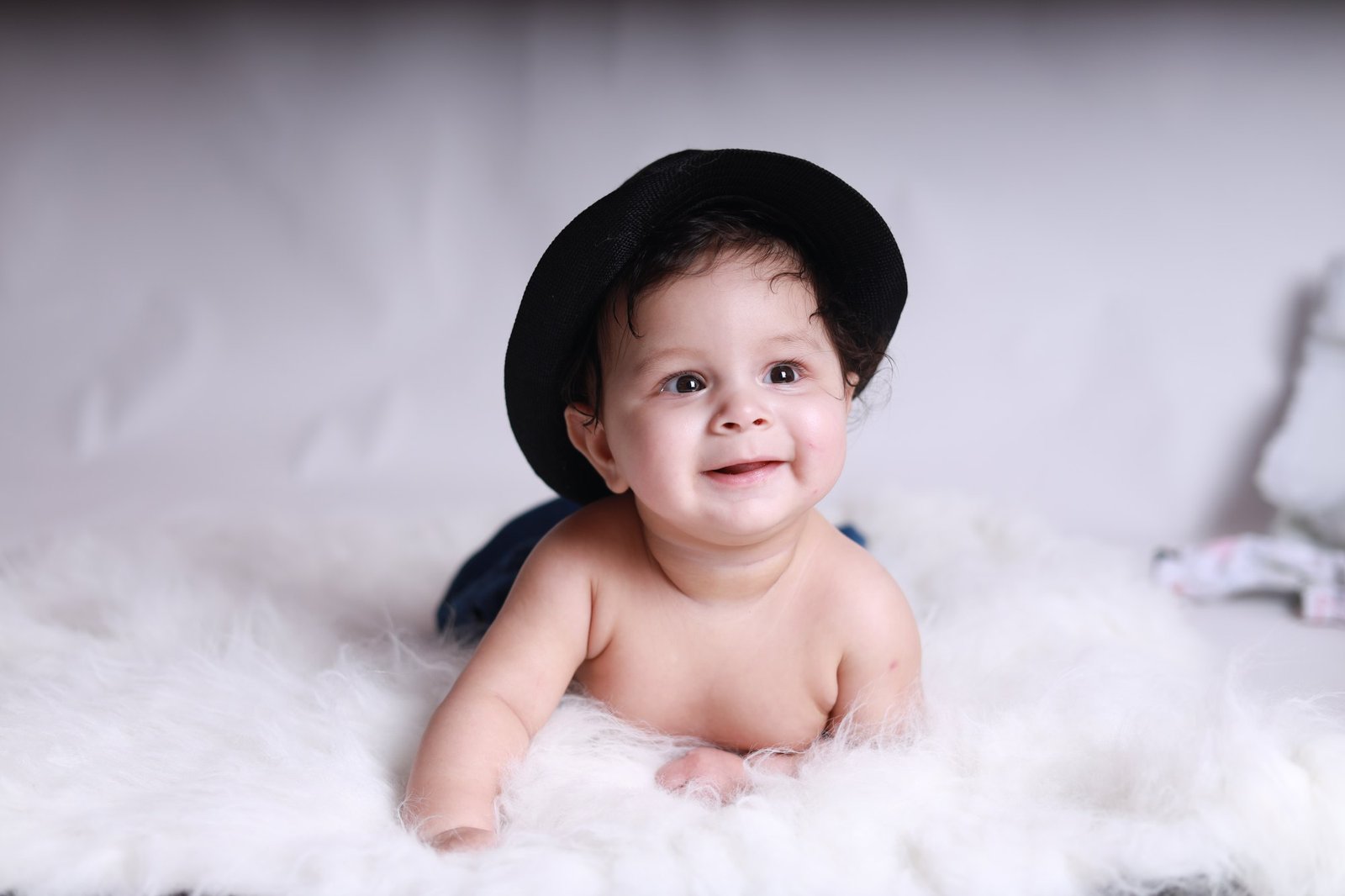 Baby in a black hat smiling during tummy time on white fur