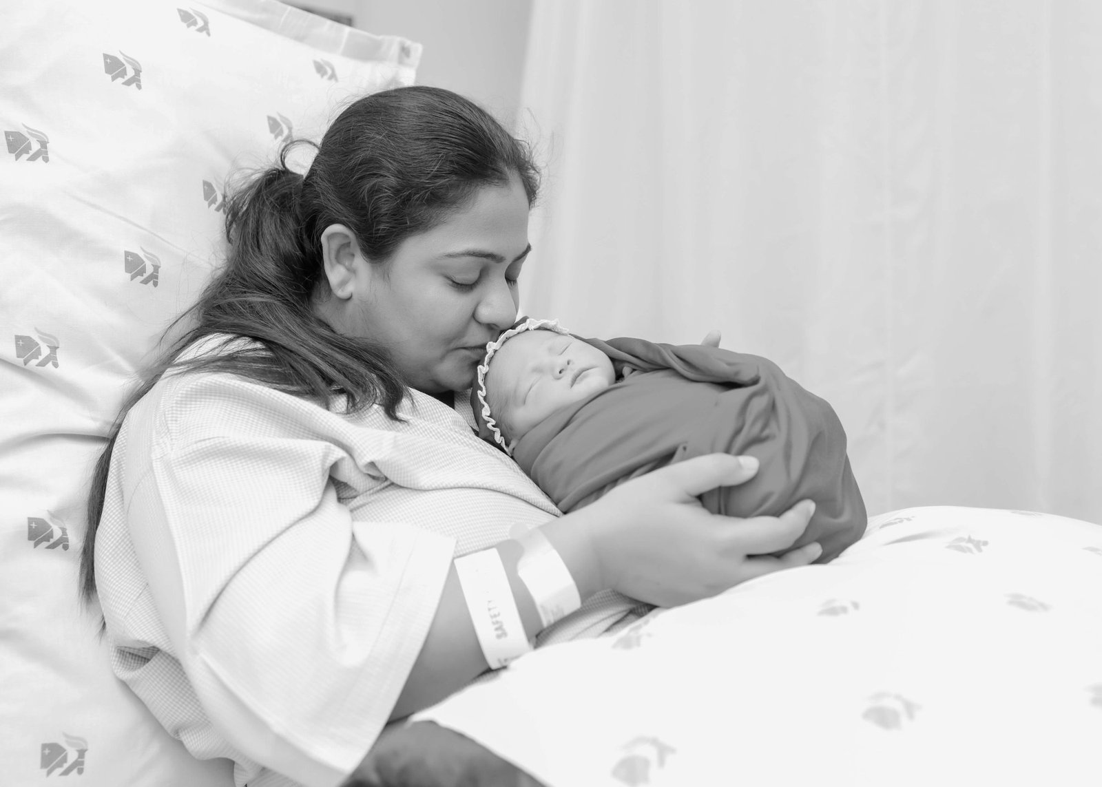 Black and white photograph of a mother resting with her newborn on the hospital bed