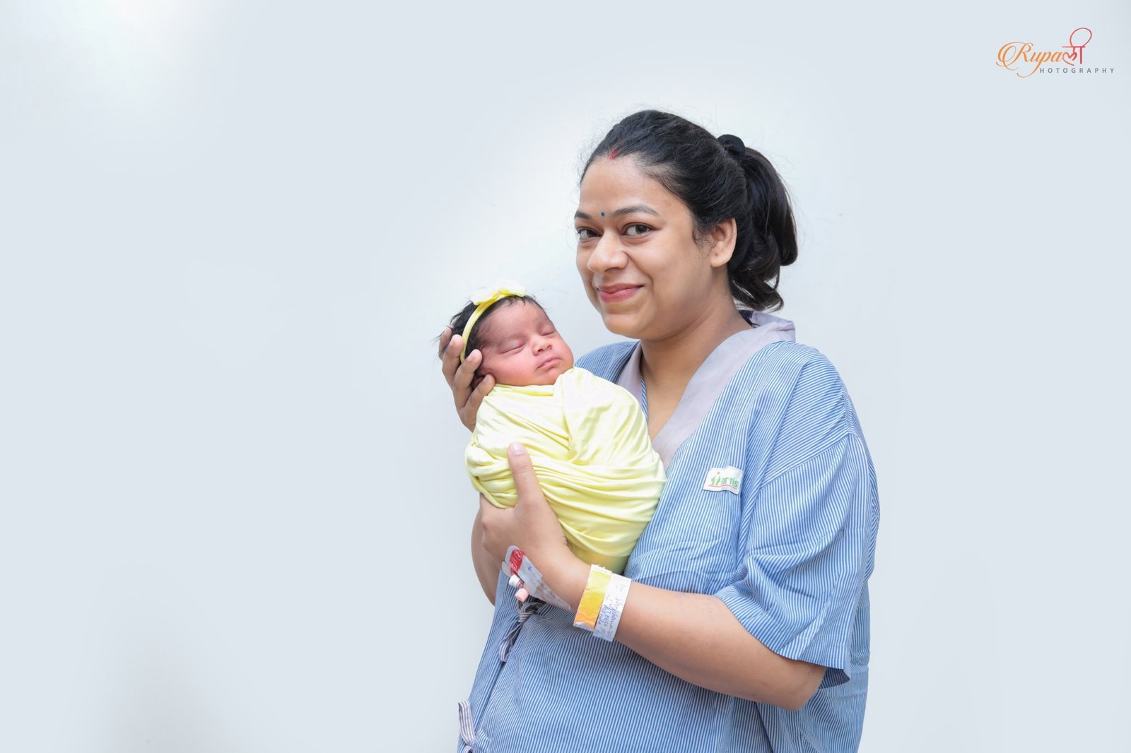 Mother in hospital gown holding her swaddled newborn