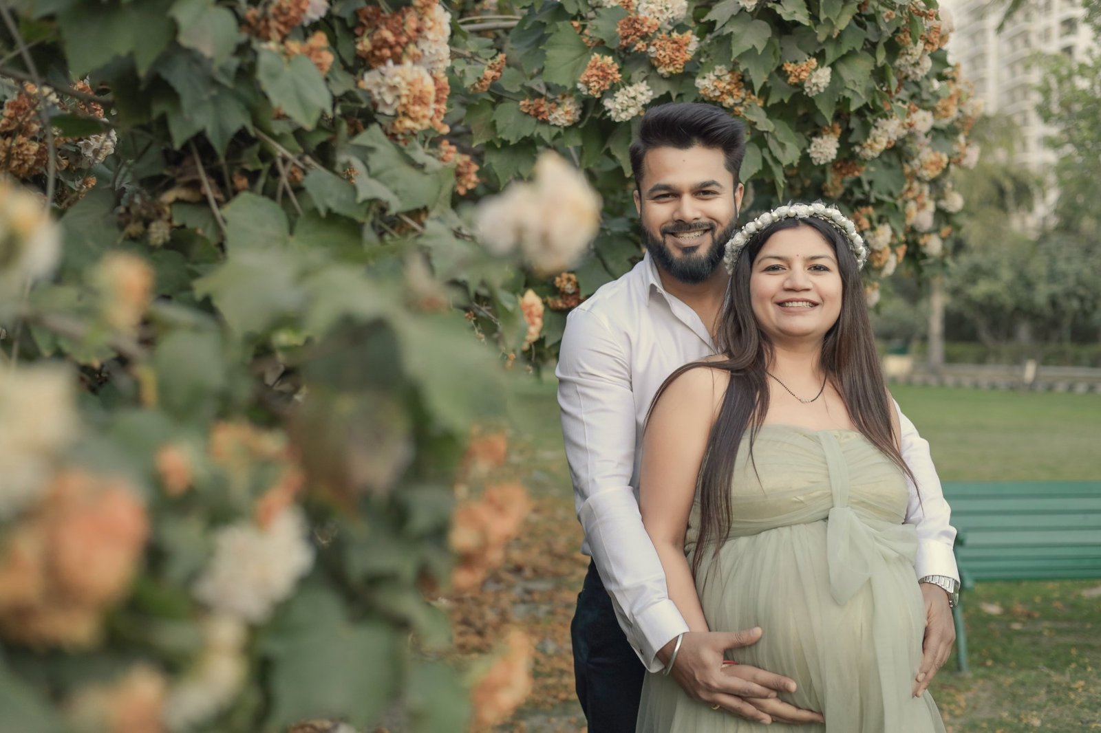 Expectant couple standing together surrounded by white flowers
