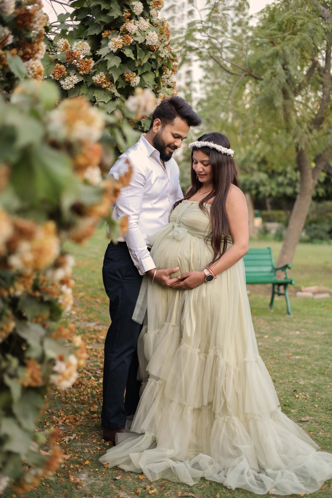 Expectant couple photographed at a floral arch outdoors