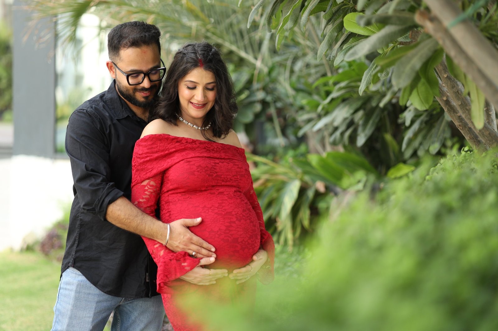 Expectant couple standing together outdoors, both hands on the bump