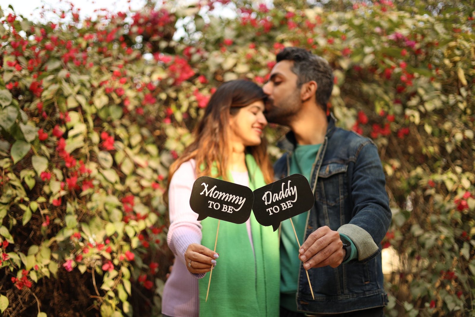 Expectant couple holding "mommy to be" and "daddy to be" signs by flowering shrubs