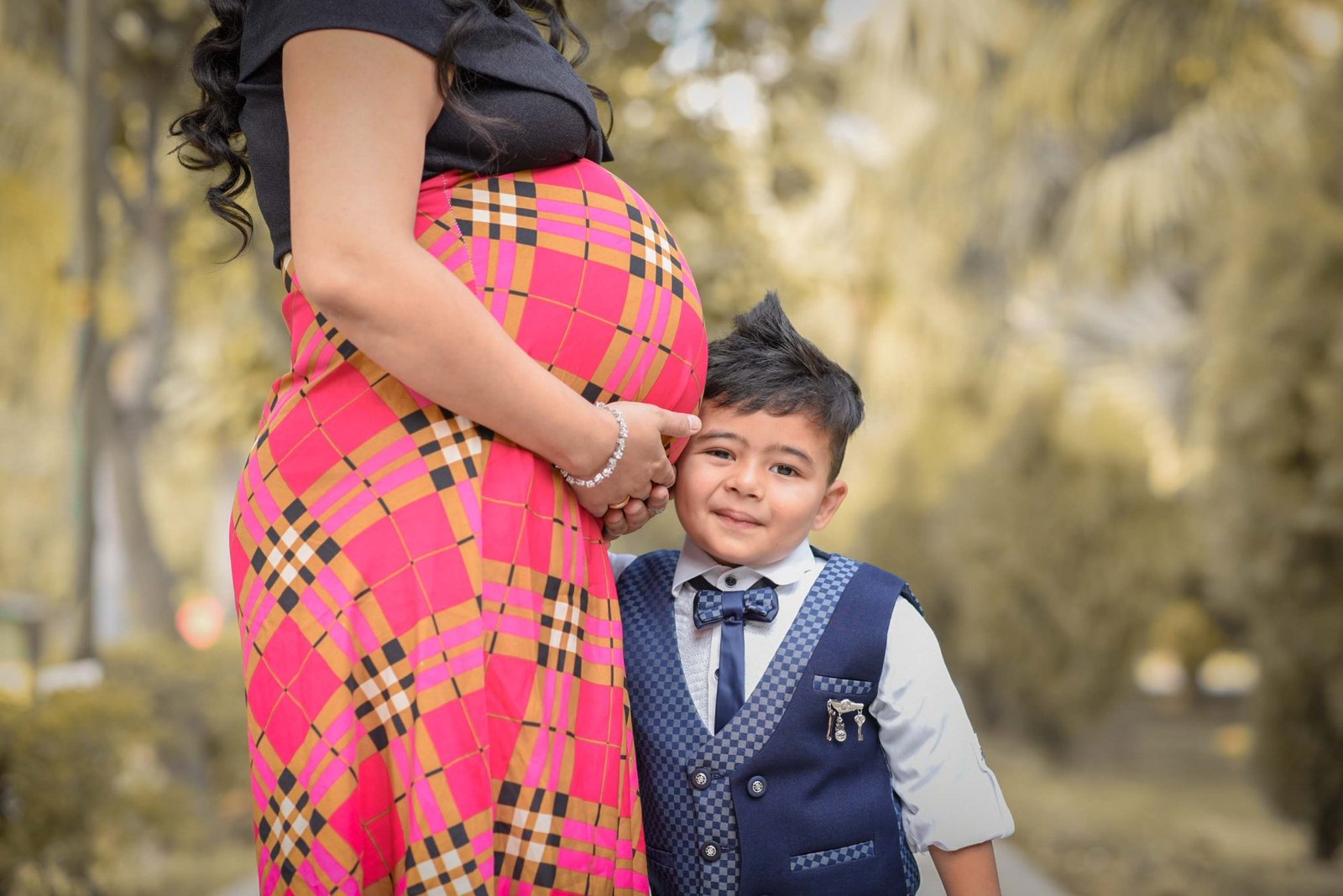 Expectant mother in a pink outfit standing with her young son in a park