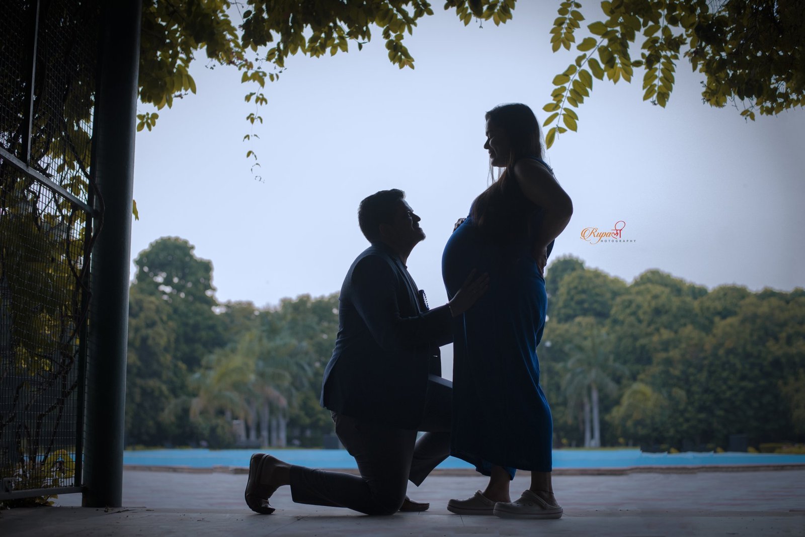 Silhouette of a partner kneeling beside an expectant mother by water at dusk
