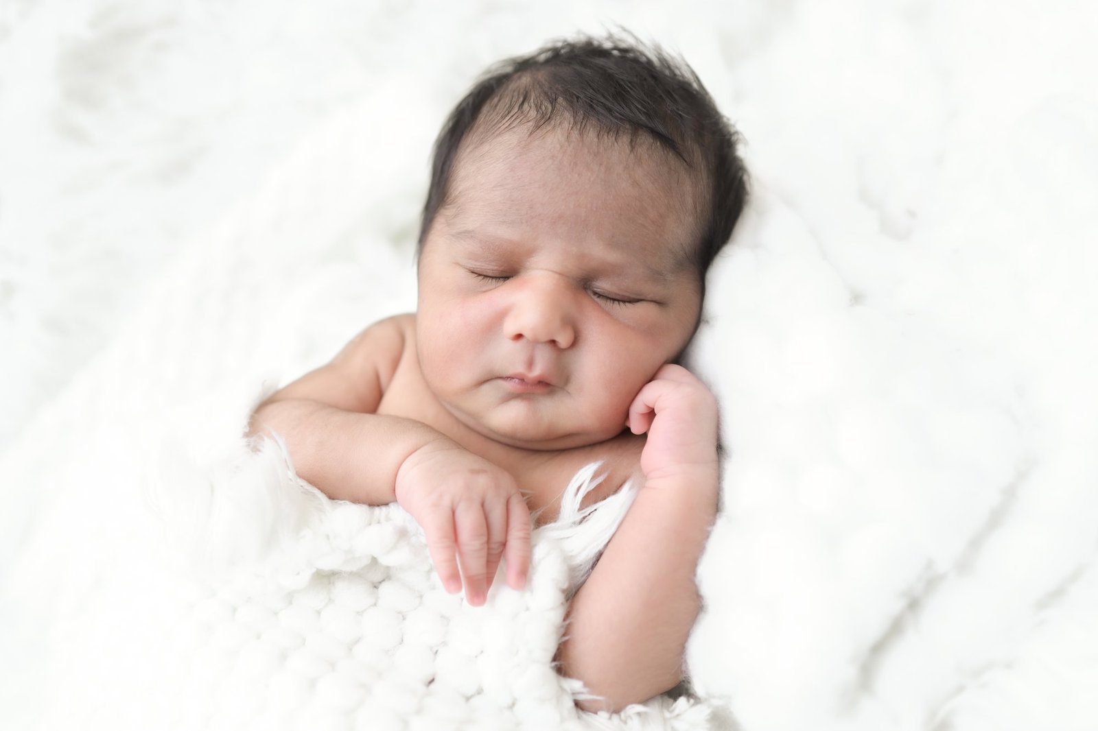 Newborn sleeping peacefully on a white fur blanket