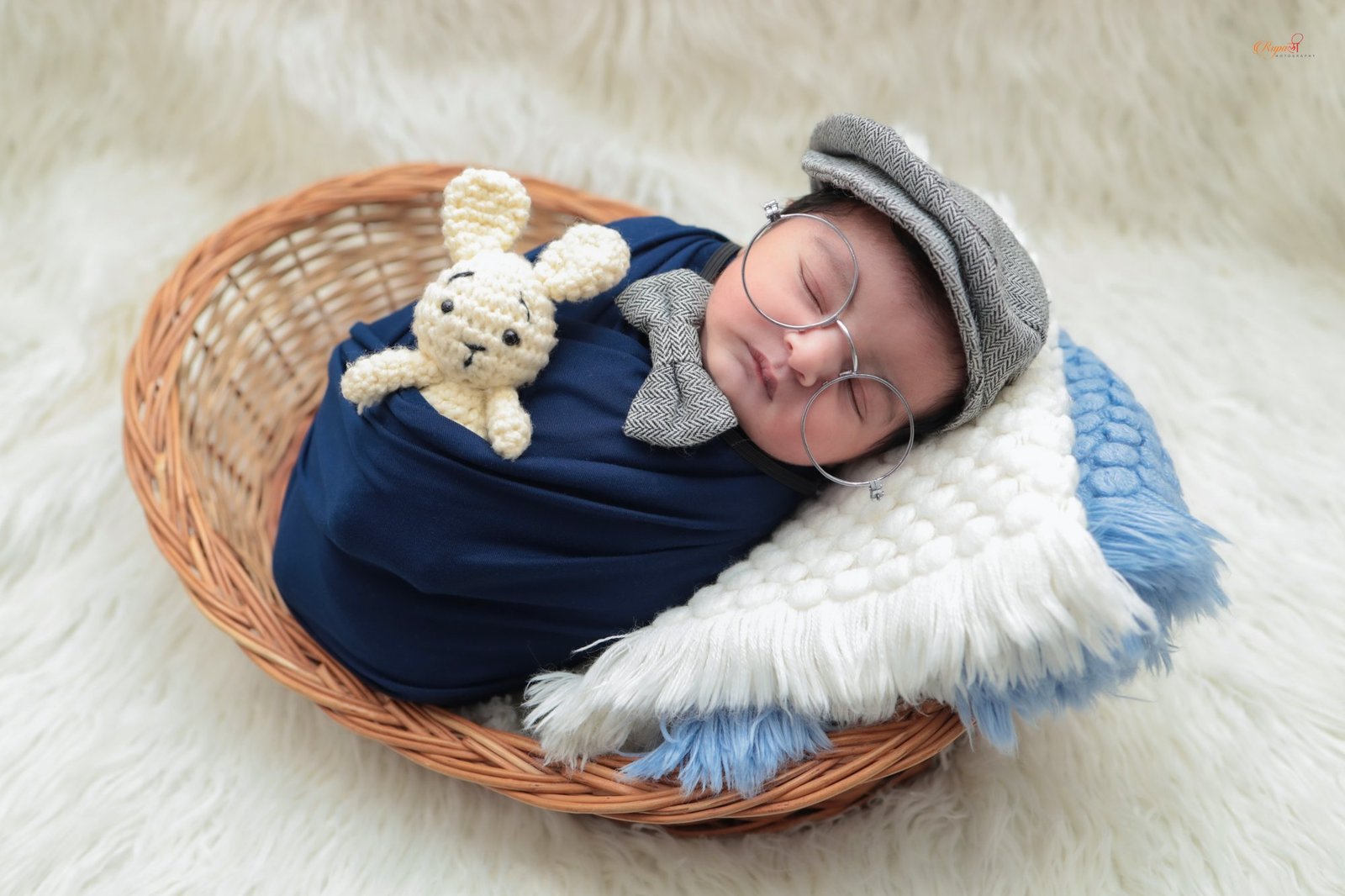 Newborn in a navy wrap asleep in a woven basket with soft wings