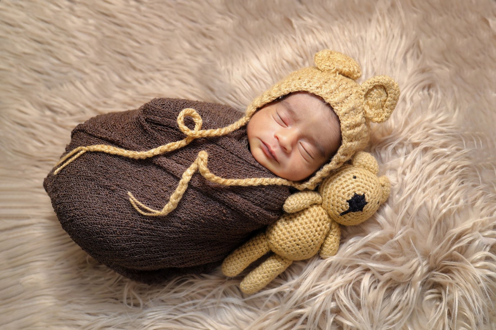 Newborn swaddled in a brown wrap and bonnet with a knitted teddy bear