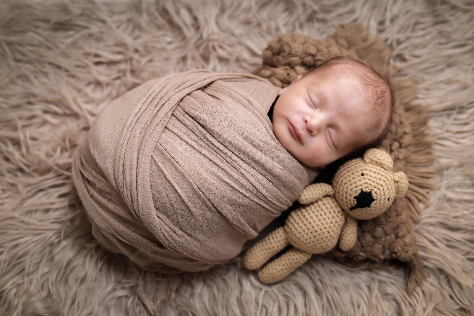 Newborn wrapped in a soft blush swaddle resting on a fur blanket