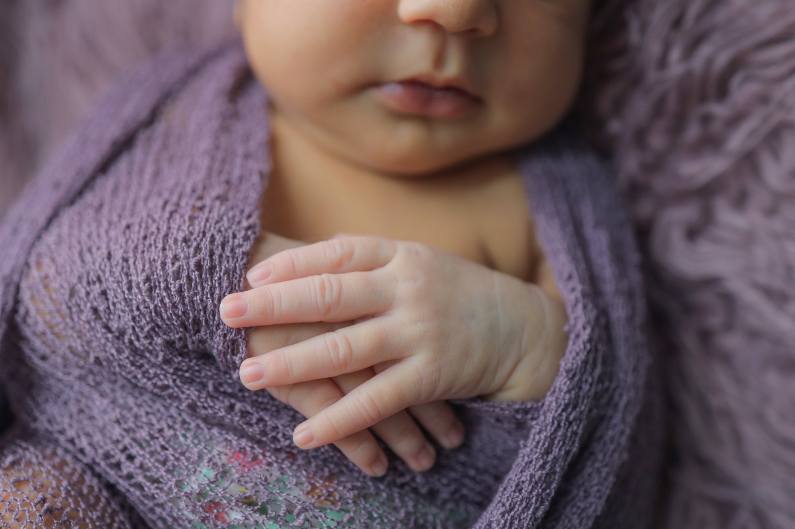 Close detail of a newborn's hand resting against a lilac wrap