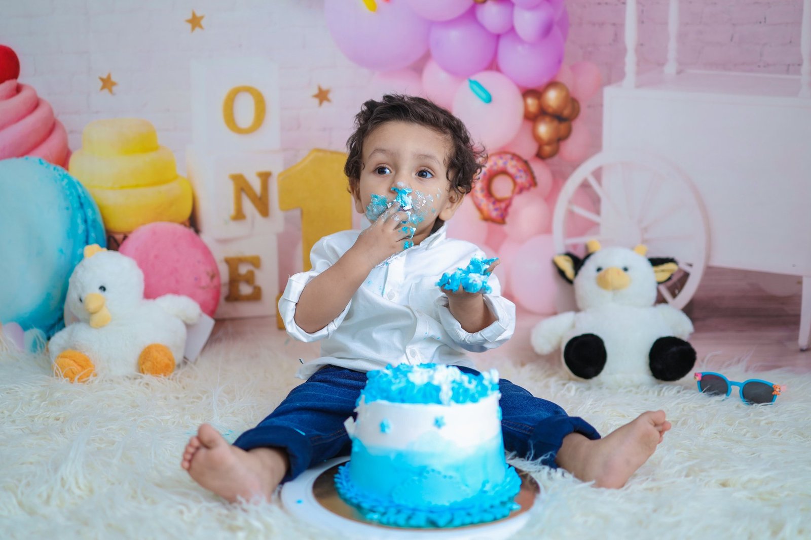 Baby seated on white fur tasting a blue iced cake