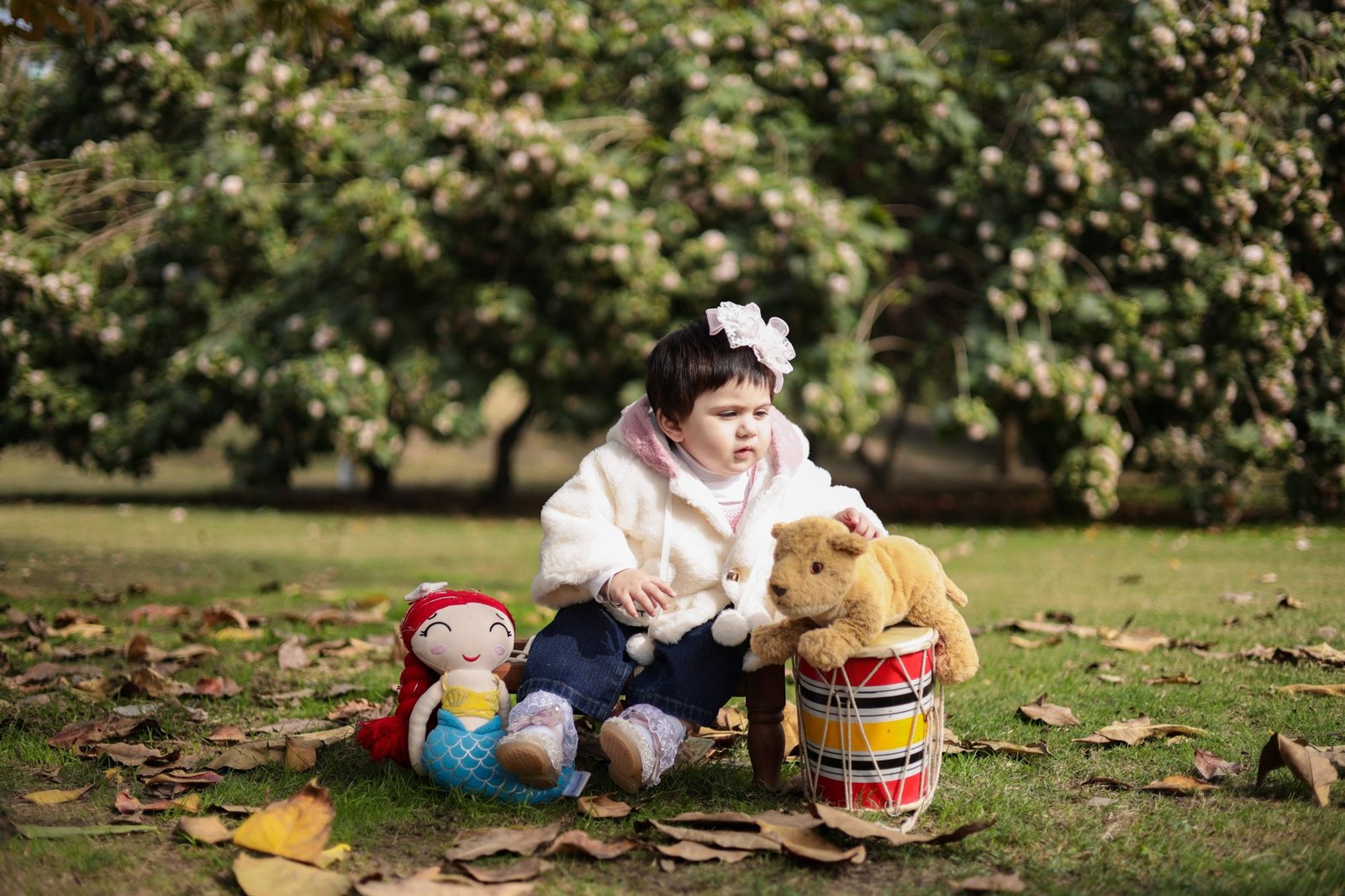 Baby in a cream jacket on a picnic blanket with toys and a drum
