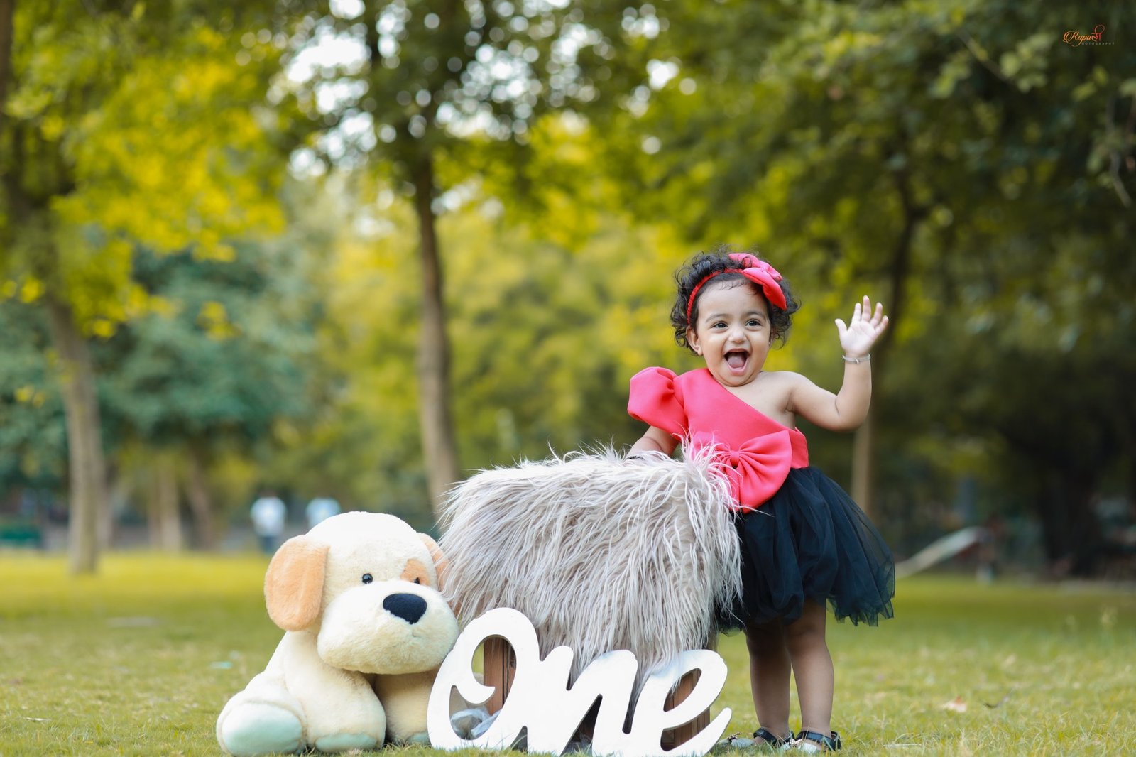 Baby in a black tutu on the grass beside a toy dog and a ONE sign