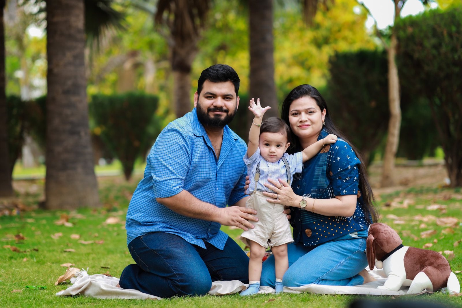 Parents seated on a picnic rug in the park with their baby