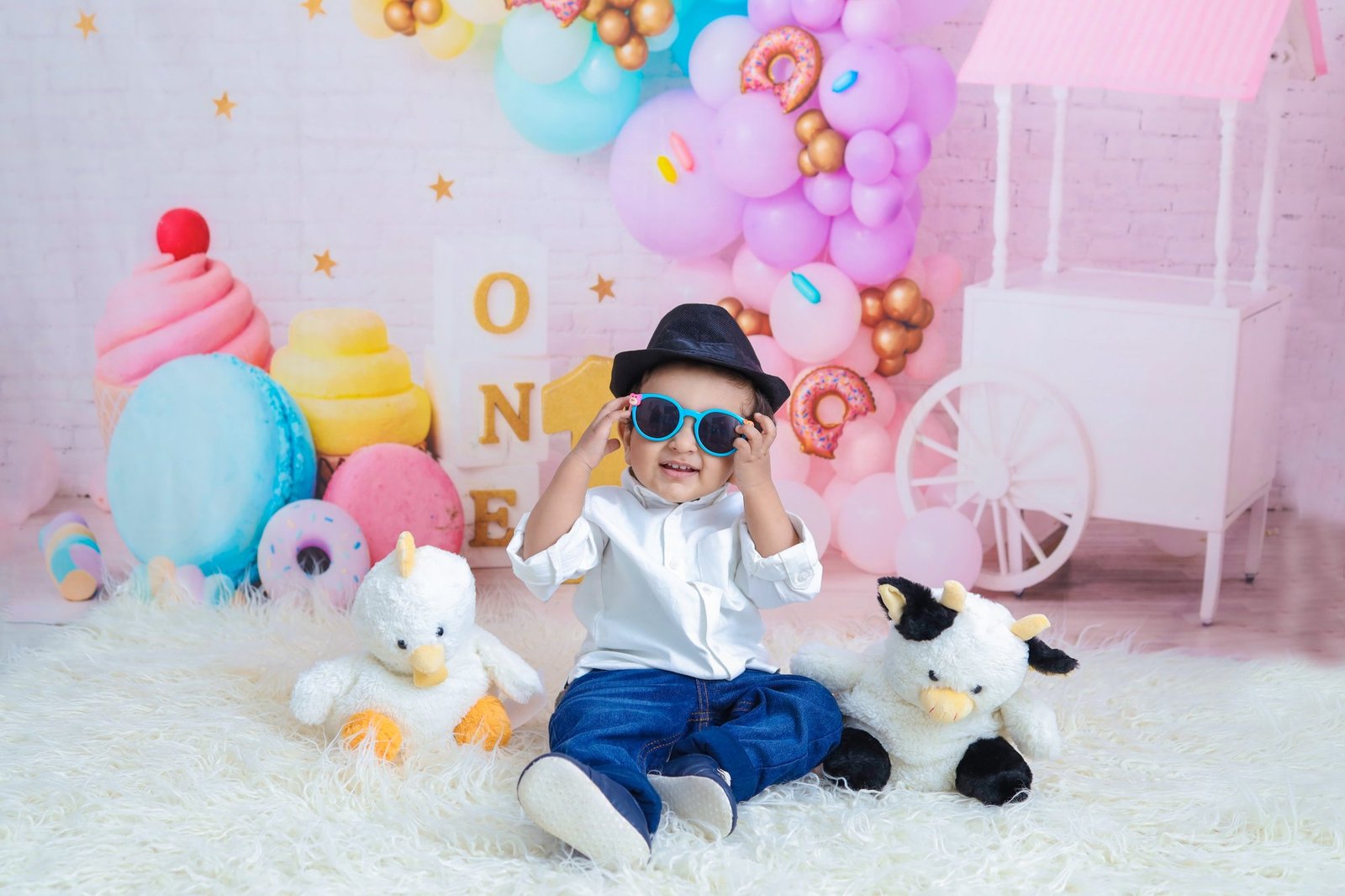 Baby in a hat and sunglasses on a styled set with a toy guitar