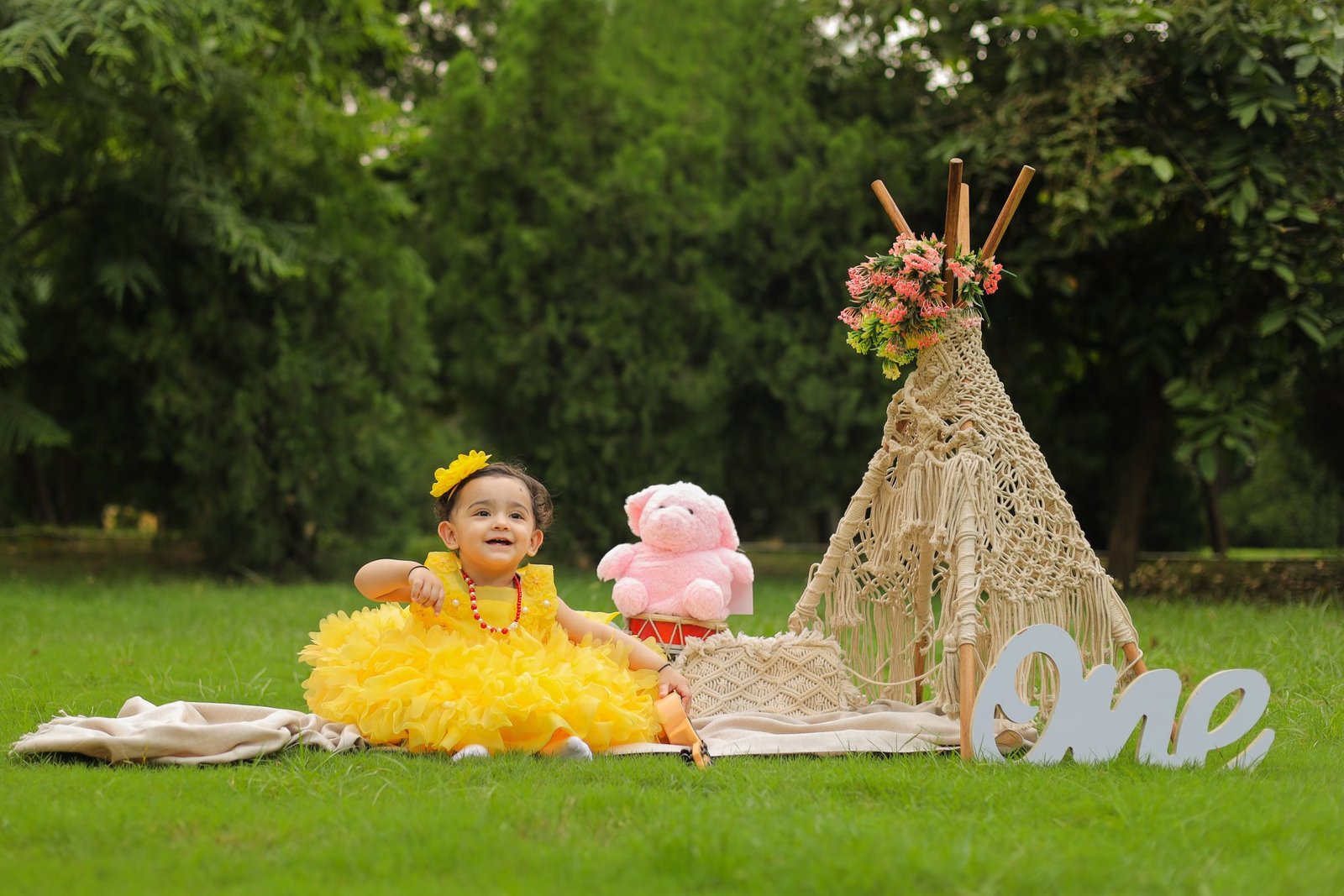 One year old in a yellow dress on a styled outdoor teepee set with a wooden ONE sign
