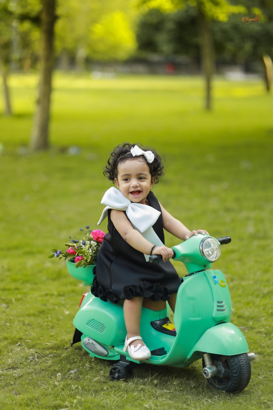 Toddler in a black dress sitting on a toy scooter on the grass