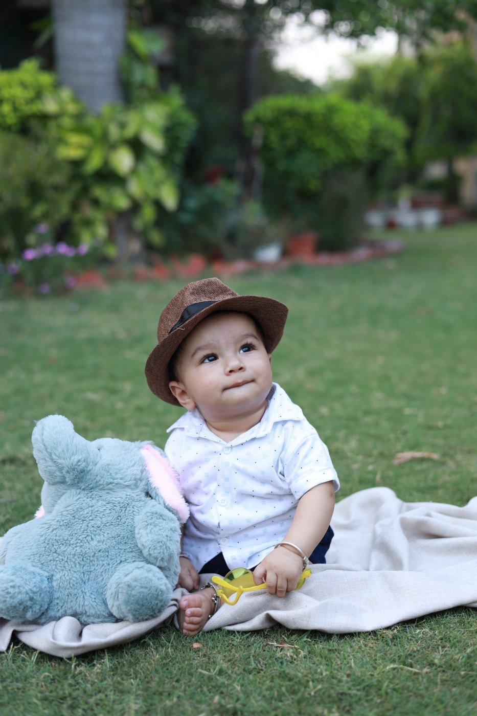 Baby sitting up unsupported on a blanket outdoors, wearing a sun hat